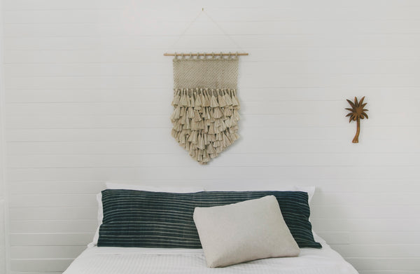 small jute wall hanging on bamboo hanging rod in bedroom above bed head